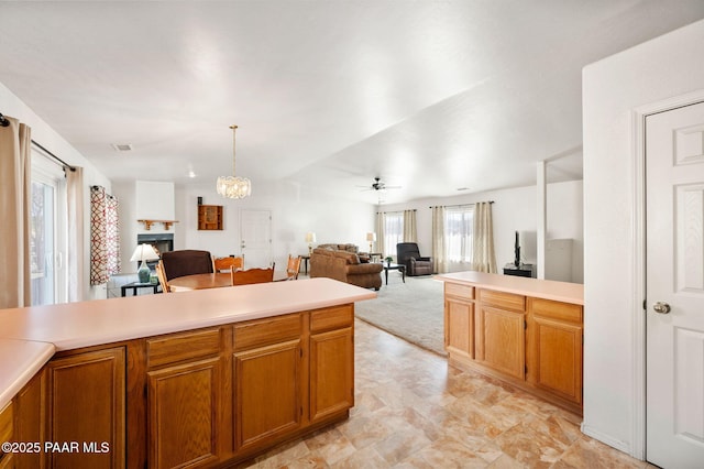 kitchen featuring open floor plan, light countertops, a lit fireplace, and brown cabinets