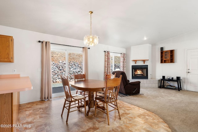 dining area featuring lofted ceiling, a tiled fireplace, an inviting chandelier, and light colored carpet