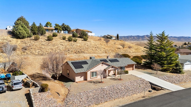 view of front facade featuring concrete driveway, stucco siding, a mountain view, and solar panels