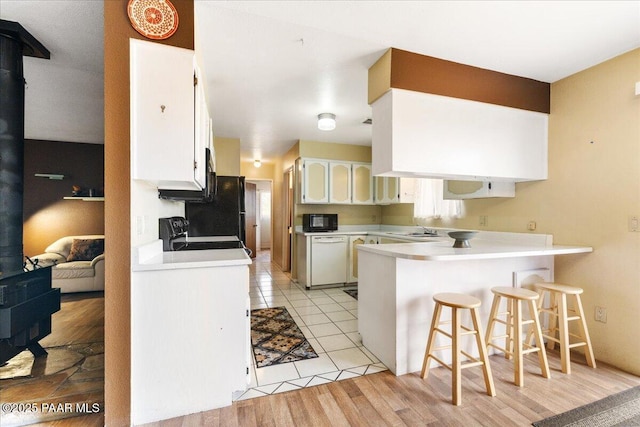 kitchen featuring white dishwasher, black microwave, a sink, a wood stove, and a peninsula