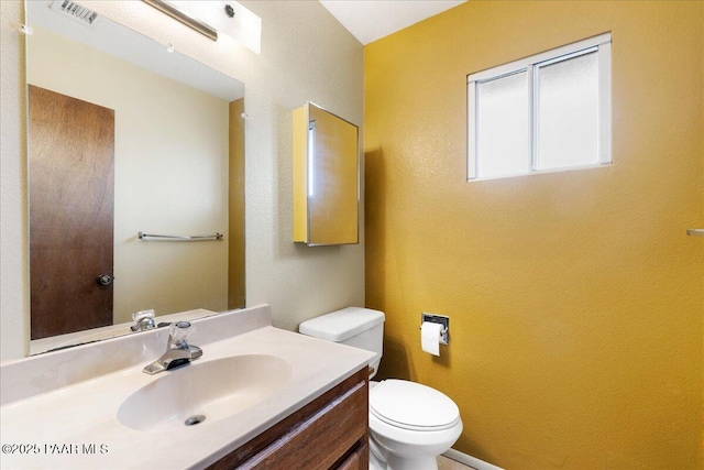 bathroom featuring vanity, a textured wall, toilet, and visible vents