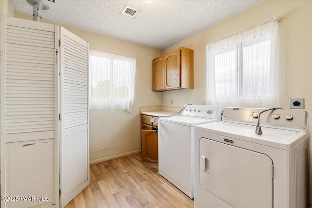 laundry area featuring separate washer and dryer, light wood finished floors, cabinet space, and visible vents