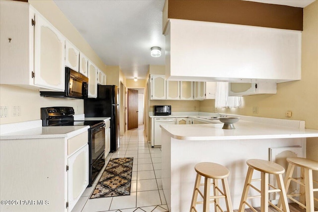 kitchen featuring white cabinets, light tile patterned flooring, a breakfast bar area, a peninsula, and black appliances