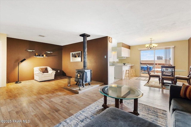 living room featuring visible vents, a chandelier, a wood stove, and light wood-type flooring