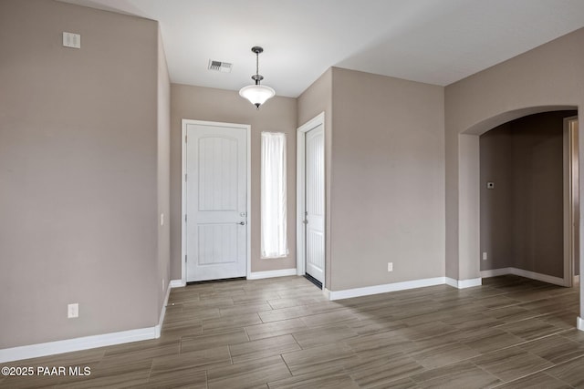 entrance foyer with arched walkways, visible vents, baseboards, and wood tiled floor