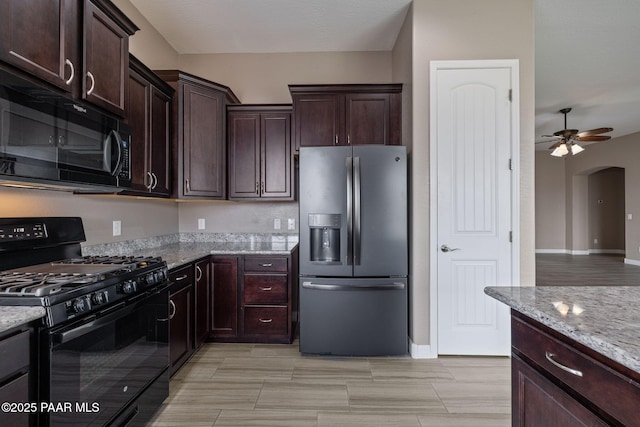 kitchen featuring black appliances, light stone countertops, arched walkways, and ceiling fan