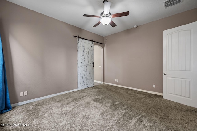 unfurnished bedroom featuring visible vents, baseboards, carpet, and a barn door