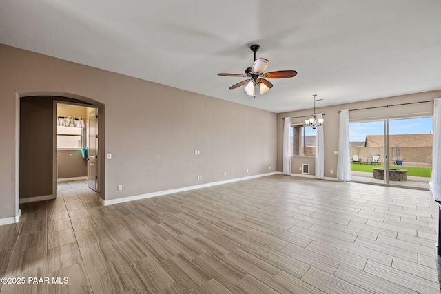 spare room featuring ceiling fan with notable chandelier, arched walkways, and baseboards