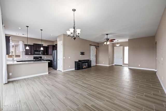 unfurnished living room featuring baseboards, wood finish floors, recessed lighting, a barn door, and ceiling fan with notable chandelier