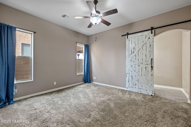 interior space with visible vents, baseboards, ceiling fan, a barn door, and carpet flooring