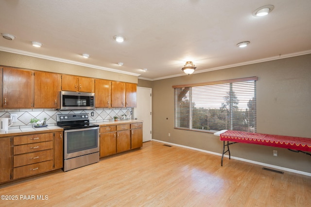 kitchen featuring crown molding, appliances with stainless steel finishes, light wood-type flooring, and decorative backsplash