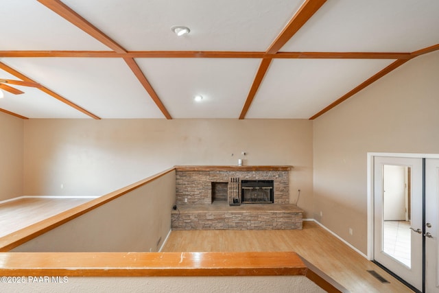 unfurnished living room with a stone fireplace, lofted ceiling, ceiling fan, and light hardwood / wood-style flooring