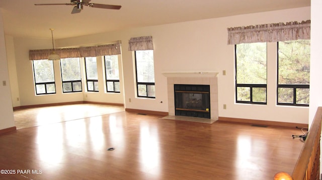 unfurnished living room featuring a tile fireplace, visible vents, baseboards, and wood finished floors