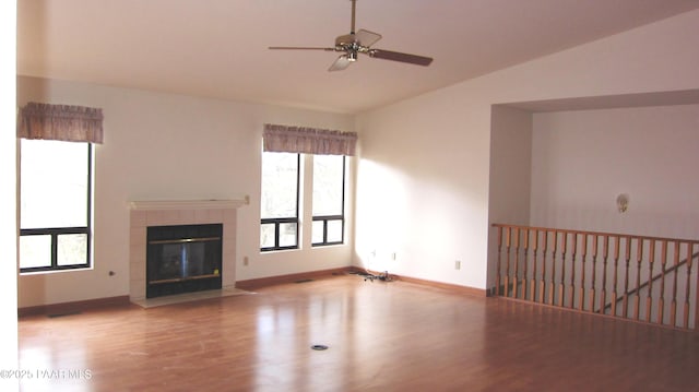 unfurnished living room with vaulted ceiling, a tiled fireplace, wood finished floors, and a wealth of natural light