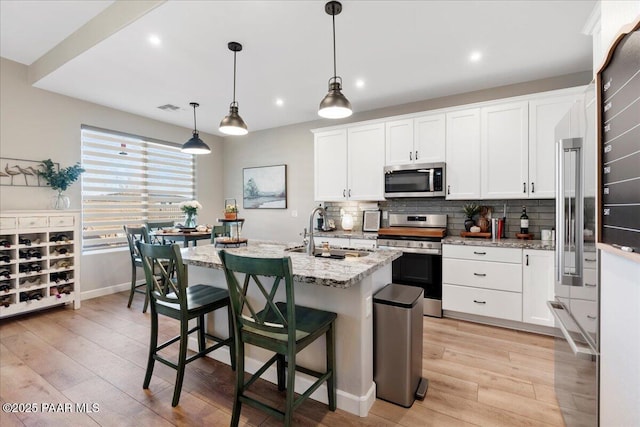 kitchen featuring decorative light fixtures, sink, white cabinetry, appliances with stainless steel finishes, and an island with sink