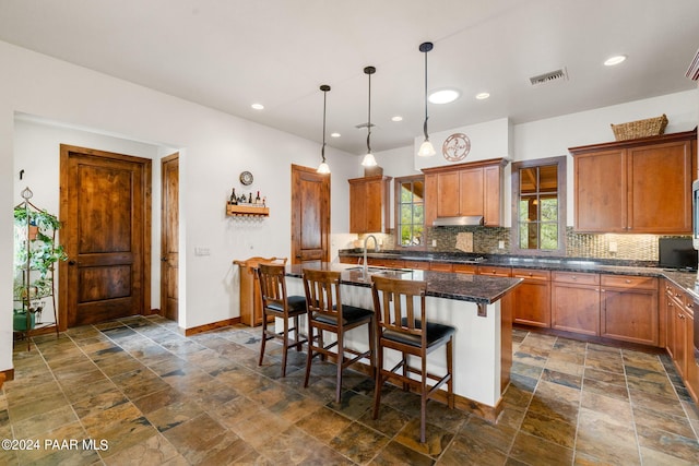 kitchen with backsplash, a breakfast bar, sink, a center island with sink, and hanging light fixtures