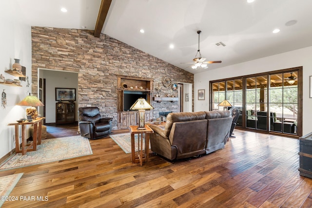 living room with ceiling fan, beam ceiling, a stone fireplace, and wood-type flooring