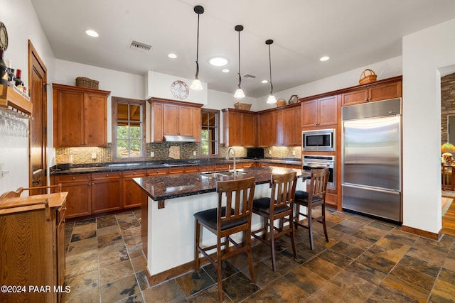 kitchen featuring sink, built in appliances, pendant lighting, a kitchen bar, and a kitchen island with sink