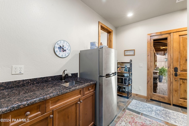 kitchen with stainless steel refrigerator, dark stone countertops, sink, and light tile patterned floors