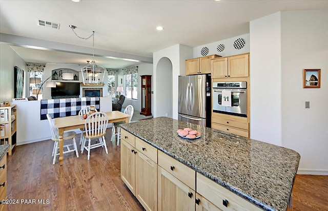 kitchen featuring light brown cabinetry, stainless steel appliances, a center island, dark hardwood / wood-style flooring, and dark stone counters