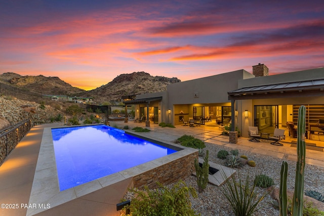 pool at dusk featuring a mountain view and a patio