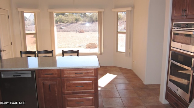 kitchen with light tile patterned floors, a breakfast bar, double oven, black dishwasher, and light stone countertops