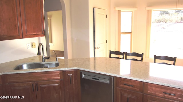 kitchen featuring stainless steel dishwasher, a breakfast bar, light stone countertops, and sink