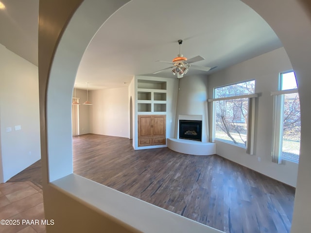 unfurnished living room featuring built in shelves, ceiling fan, and dark hardwood / wood-style flooring