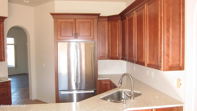 kitchen featuring stainless steel refrigerator, tile patterned flooring, light stone countertops, and sink