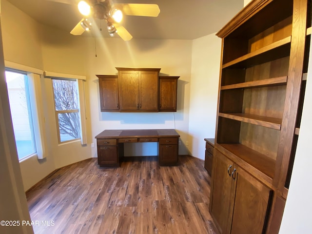 unfurnished office with built in desk, dark wood-type flooring, and ceiling fan