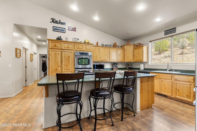 kitchen with light wood finished floors, dark countertops, a sink, vaulted ceiling, and a center island