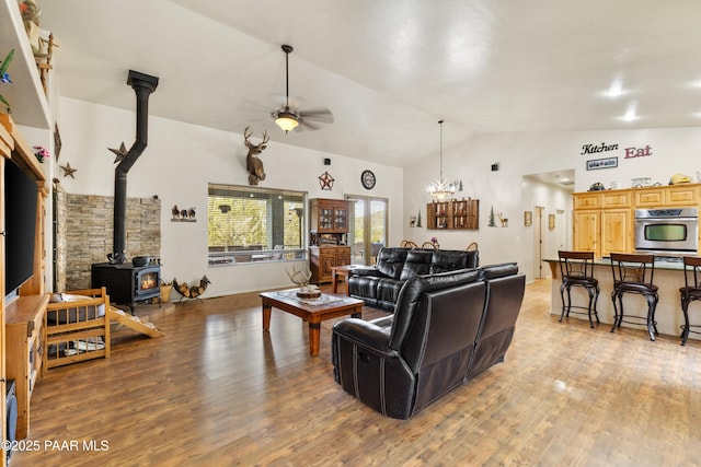 living area with a ceiling fan, high vaulted ceiling, light wood-style floors, and a wood stove