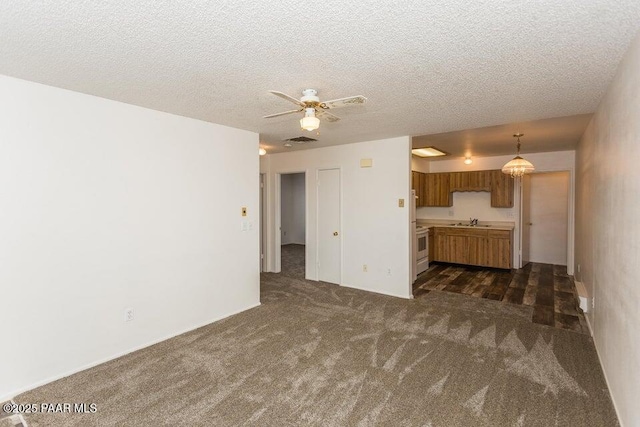 unfurnished living room with visible vents, dark carpet, a textured ceiling, a ceiling fan, and a sink