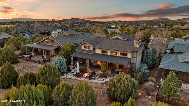 back of property at dusk with a fire pit, a patio, a shingled roof, and a residential view