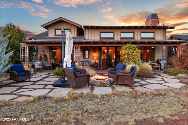 back of house at dusk with a patio, board and batten siding, a chimney, and an outdoor living space with a fire pit