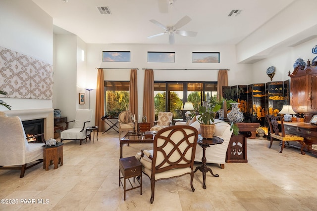 dining area with a ceiling fan, a glass covered fireplace, visible vents, and a high ceiling