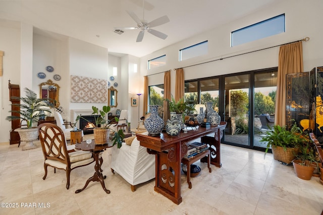 interior space with a towering ceiling, a warm lit fireplace, visible vents, and a ceiling fan