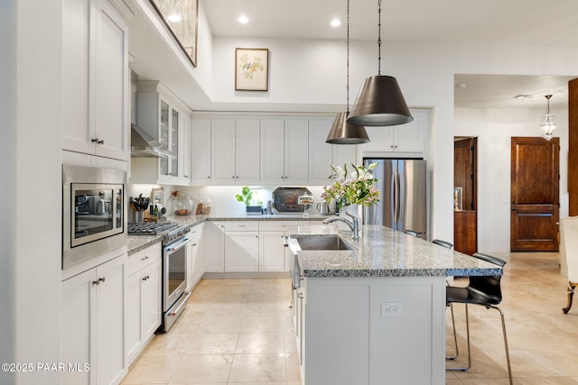 kitchen with a sink, a kitchen breakfast bar, appliances with stainless steel finishes, light stone countertops, and an island with sink