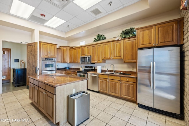 kitchen with appliances with stainless steel finishes, a center island, light tile patterned floors, and a sink