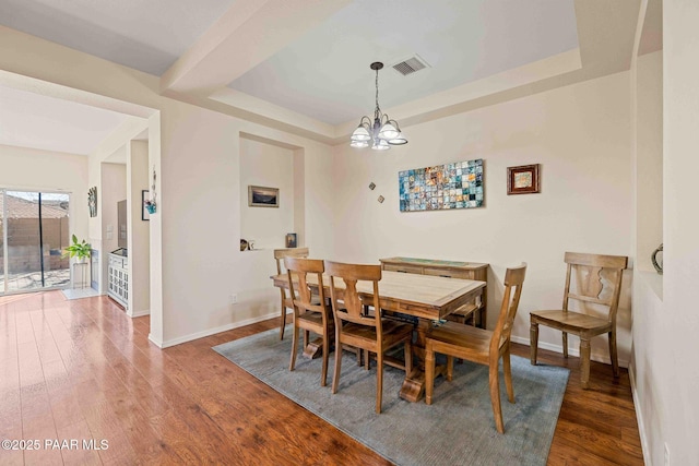 dining area with a tray ceiling, wood finished floors, visible vents, and baseboards