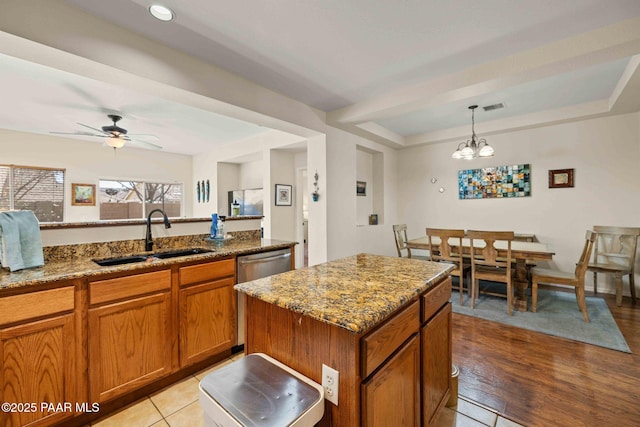 kitchen featuring light stone countertops, brown cabinetry, visible vents, a sink, and ceiling fan with notable chandelier