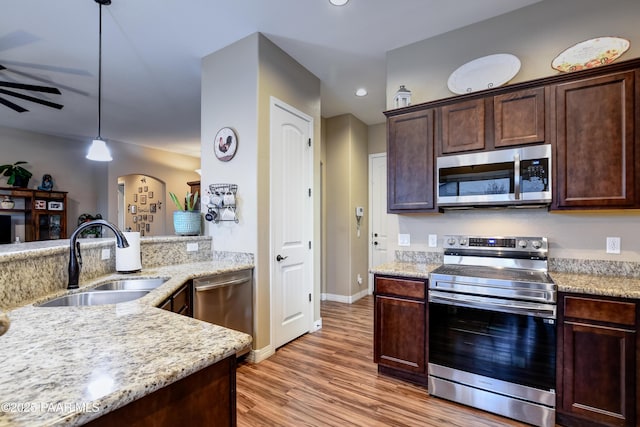 kitchen featuring appliances with stainless steel finishes, a sink, light wood-style flooring, and light stone countertops