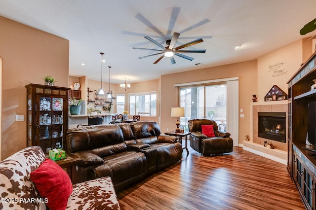 living room with visible vents, a tiled fireplace, wood finished floors, ceiling fan with notable chandelier, and recessed lighting