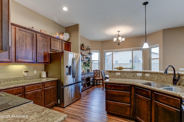 kitchen featuring wood finished floors, a sink, stainless steel refrigerator with ice dispenser, light stone countertops, and decorative light fixtures