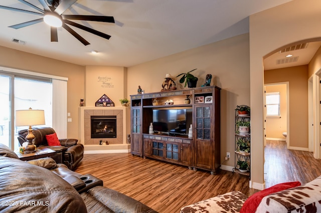 living room featuring arched walkways, a fireplace, visible vents, wood finished floors, and baseboards