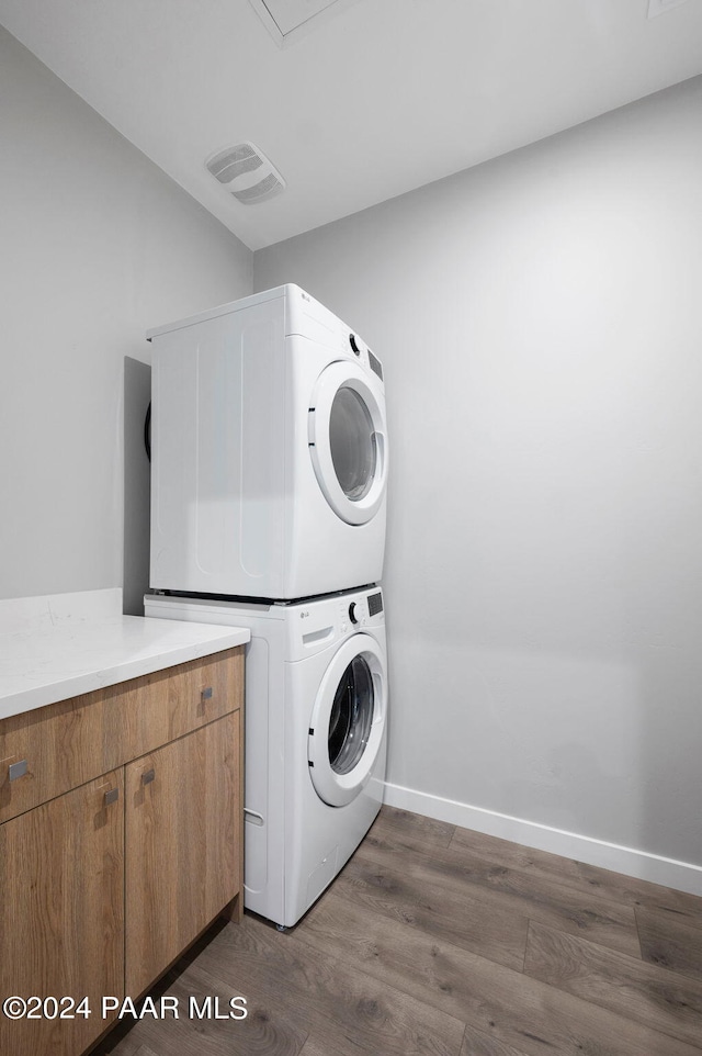 laundry room with baseboards, stacked washer and dryer, dark wood-style floors, visible vents, and cabinet space
