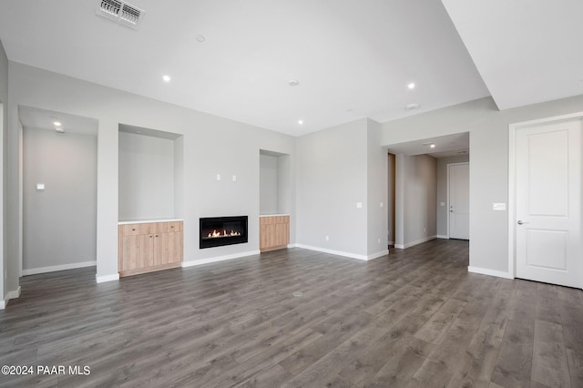 unfurnished living room with dark wood-type flooring, baseboards, a glass covered fireplace, and visible vents