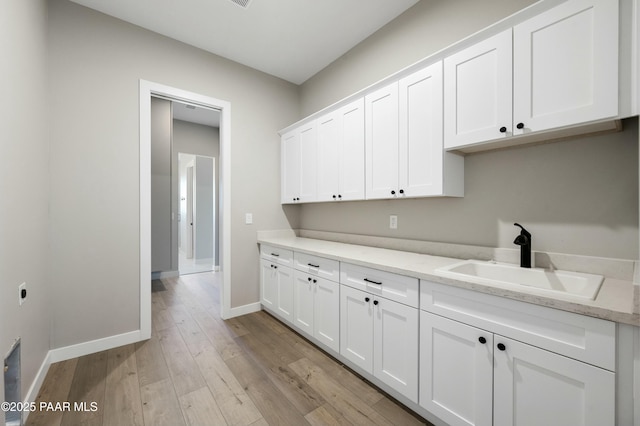 kitchen featuring white cabinetry, sink, light stone countertops, and light hardwood / wood-style floors