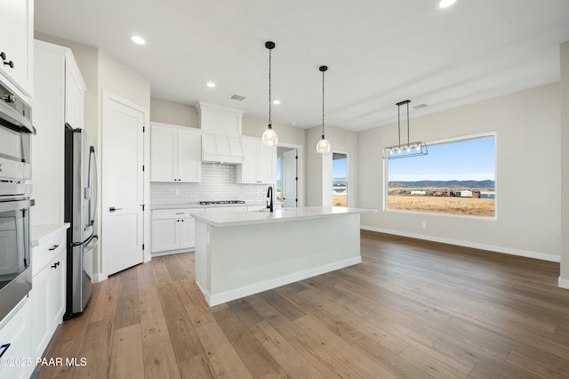 kitchen featuring white cabinetry, stainless steel appliances, hanging light fixtures, and a center island with sink