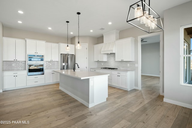 kitchen with appliances with stainless steel finishes, a kitchen island with sink, white cabinets, and decorative light fixtures